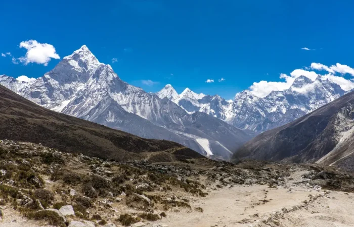 A climber trekking along the snowy ridge of Lobuche East Peak, surrounded by vast Himalayan landscapes under a blue sky.