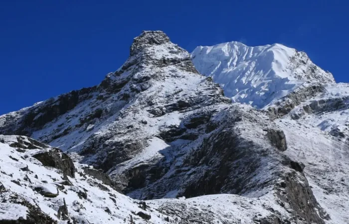 Climbers on the summit of Lobuche East Peak with sweeping views of the snow-covered Himalayas under a bright, clear sky.