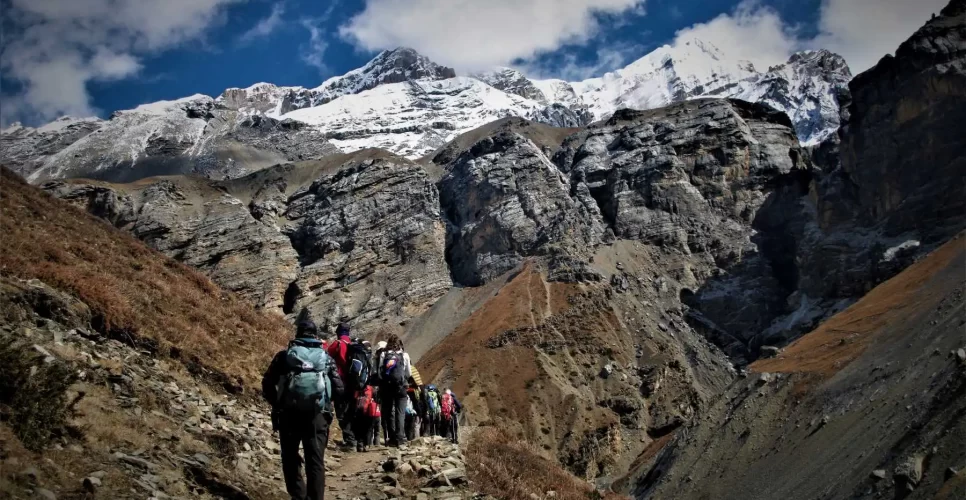Trekker navigating steep rocky trail on Nepal trek challenge with snow-capped Himalayan peaks in background