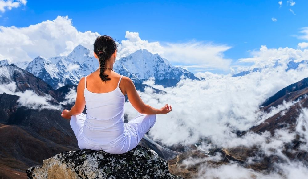 Girl meditating above the Himalayan mountains at a Himalayan yoga retreat experience
