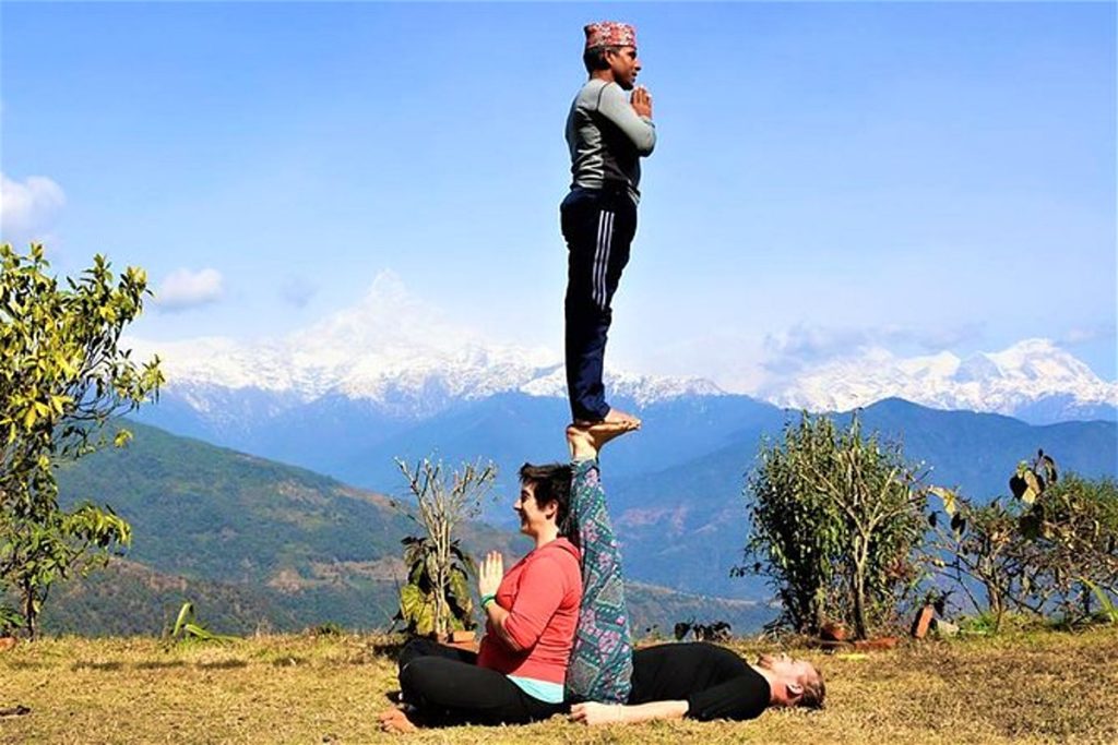 Three people performing yoga poses outdoors with Himalayan mountain views at affordable yoga retreats in Nepal