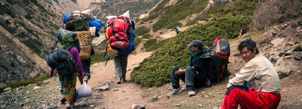 Local guides and porters trekking in the Himalayas, highlighting trekking with local agency vs international company in Nepal