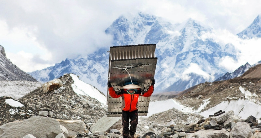 Sherpa porter carrying supplies along a Himalayan trekking trail in Nepal