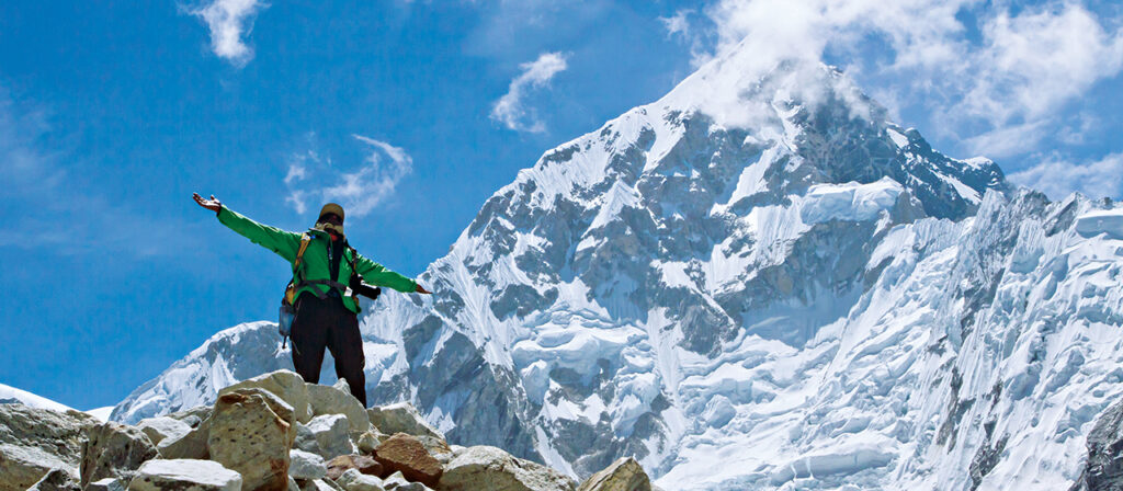 Trekker walking toward Everest Base Camp with snow-covered Himalayan peaks, wearing Everest base camp clothing and carrying Himalayan trekking gear on the EBC trail in Nepal