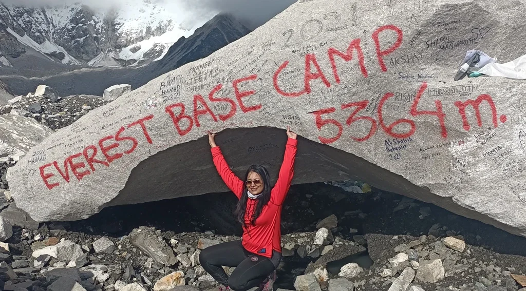 Everest Base Camp Trek Location Female trekker posing at Sagarmatha (Everest) Base Camp location with prayer flags, snowy peaks, and the Khumbu Glacier during the Everest Base Camp trek in Nepal