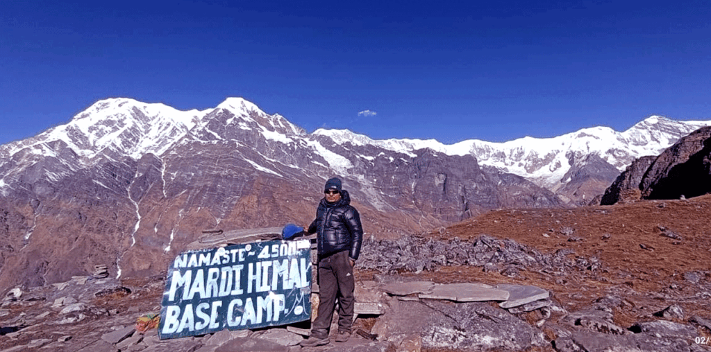 Trekker posing in front of the Mardi Himal Base Camp signboard in Nepal