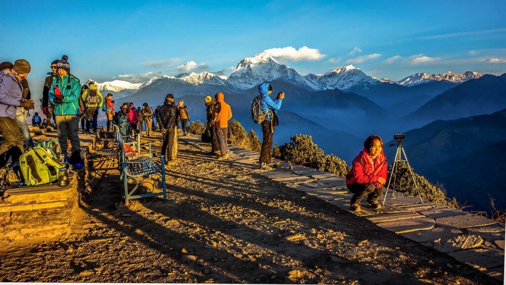 Trekkers taking photos and enjoying the sunrise at Poon Hill viewpoint with panoramic views of the Annapurna and Dhaulagiri mountain ranges in Nepal.