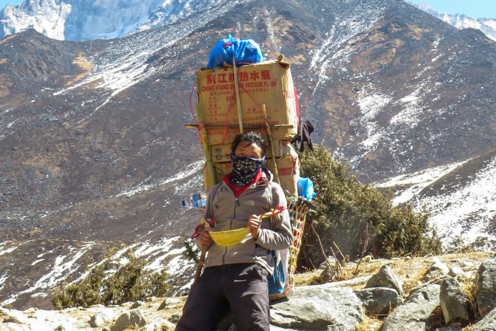 A porter from a trusted Nepal Trek Agency carrying trekking gear on a Himalayan trail in Nepal.