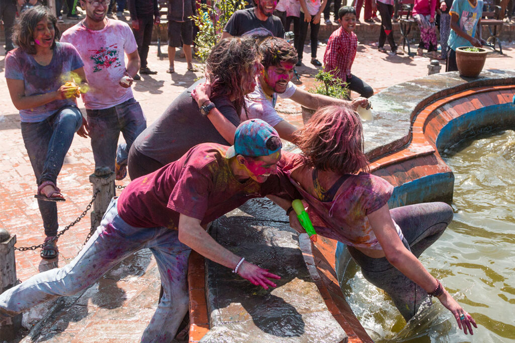 Travelers covered in traditional colored powder celebrating the Holi festival with local friends in Nepal.