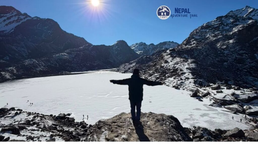 A trekker posing at a high-altitude viewpoint overlooking the frozen Gosaikunda Lake and snow-capped Himalayas during the Gosaikunda trek.