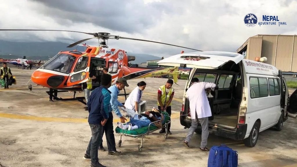 A sick trekker on a stretcher being carefully transferred from a medical helicopter to a ground ambulance, illustrating the final step in a Heli Ambulance Nepal emergency air medical rescue.