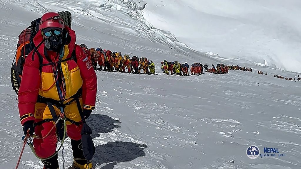 A line of mountaineers wearing colorful heavy winter gear and backpacks as they trek up a steep, snow-covered ridge, illustrating what it takes about mount everest expeditions.
