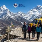 Four travelers and a pilot standing near a yellow and blue helicopter on a mountain ridge during a Himalayan Helicopter Tour Nepal, with Mount Everest and Ama Dablam in the background.