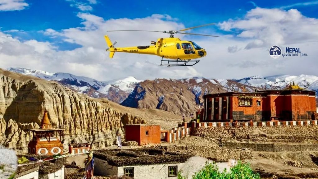 A bright yellow sightseeing helicopter flying above the unique arid landscape, red rock cliffs, and traditional villages of Upper Mustang, with snow-capped Himalayan mountains in the distance during a Mustang Helicopter Tour Nepal.